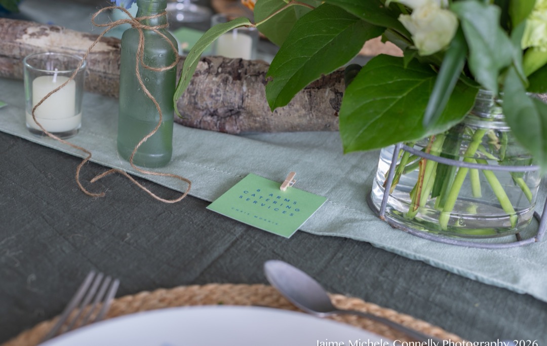 A table set with glassware, candles, greenery and place cards