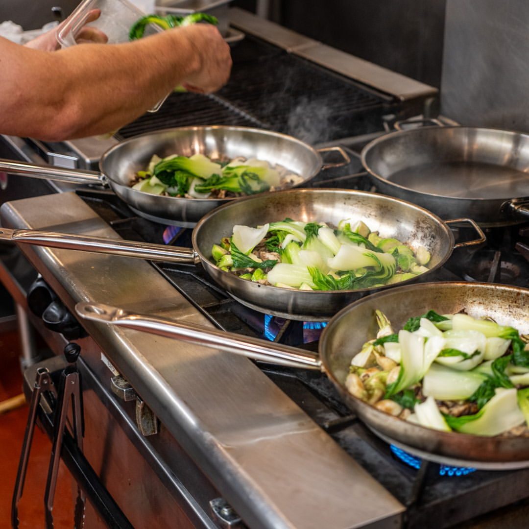 Bok choy sautéing in pans on a Hive kitchen range