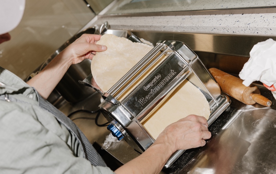 A Maker feeding dough through a pasta roller