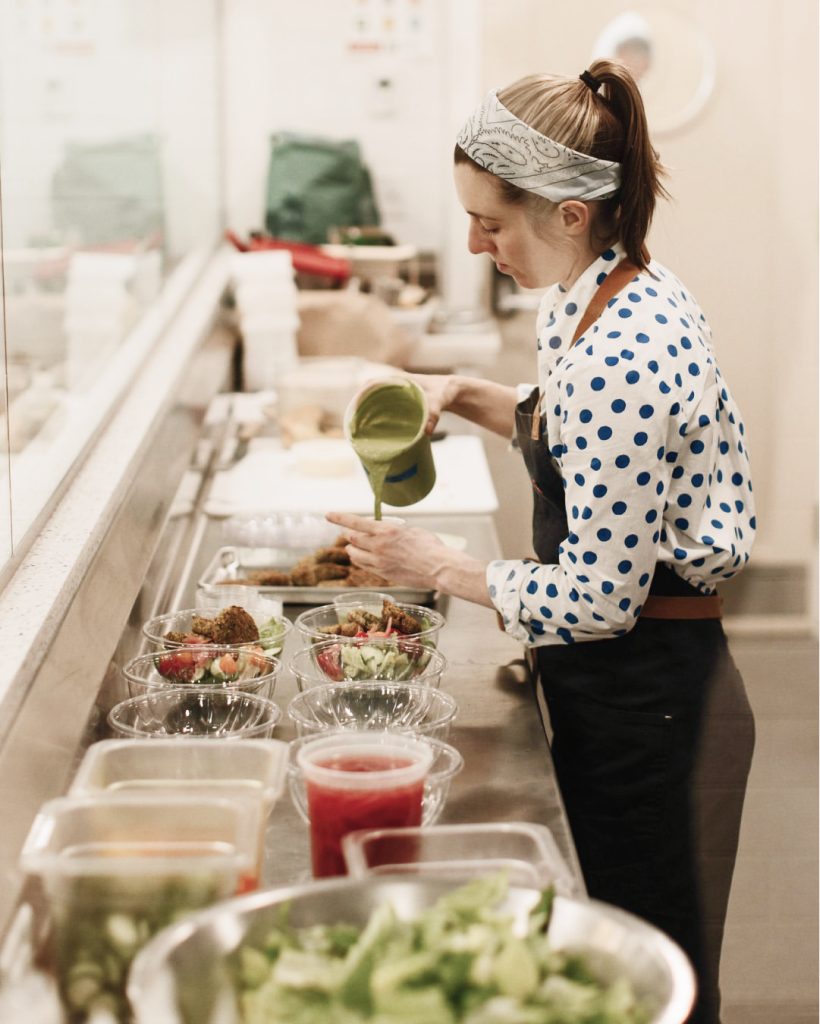 A Maker portioning a dressing over salads in a Hive kitchen