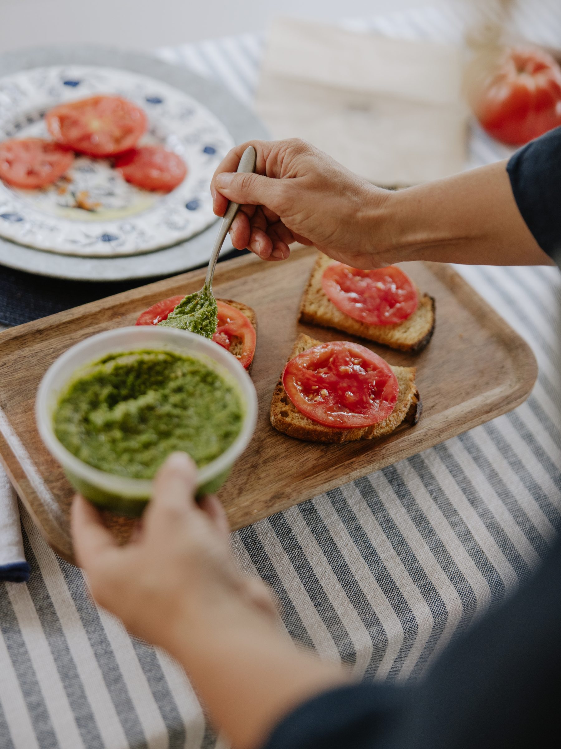 Pesto spooned onto tomato toasts on a wooden tray