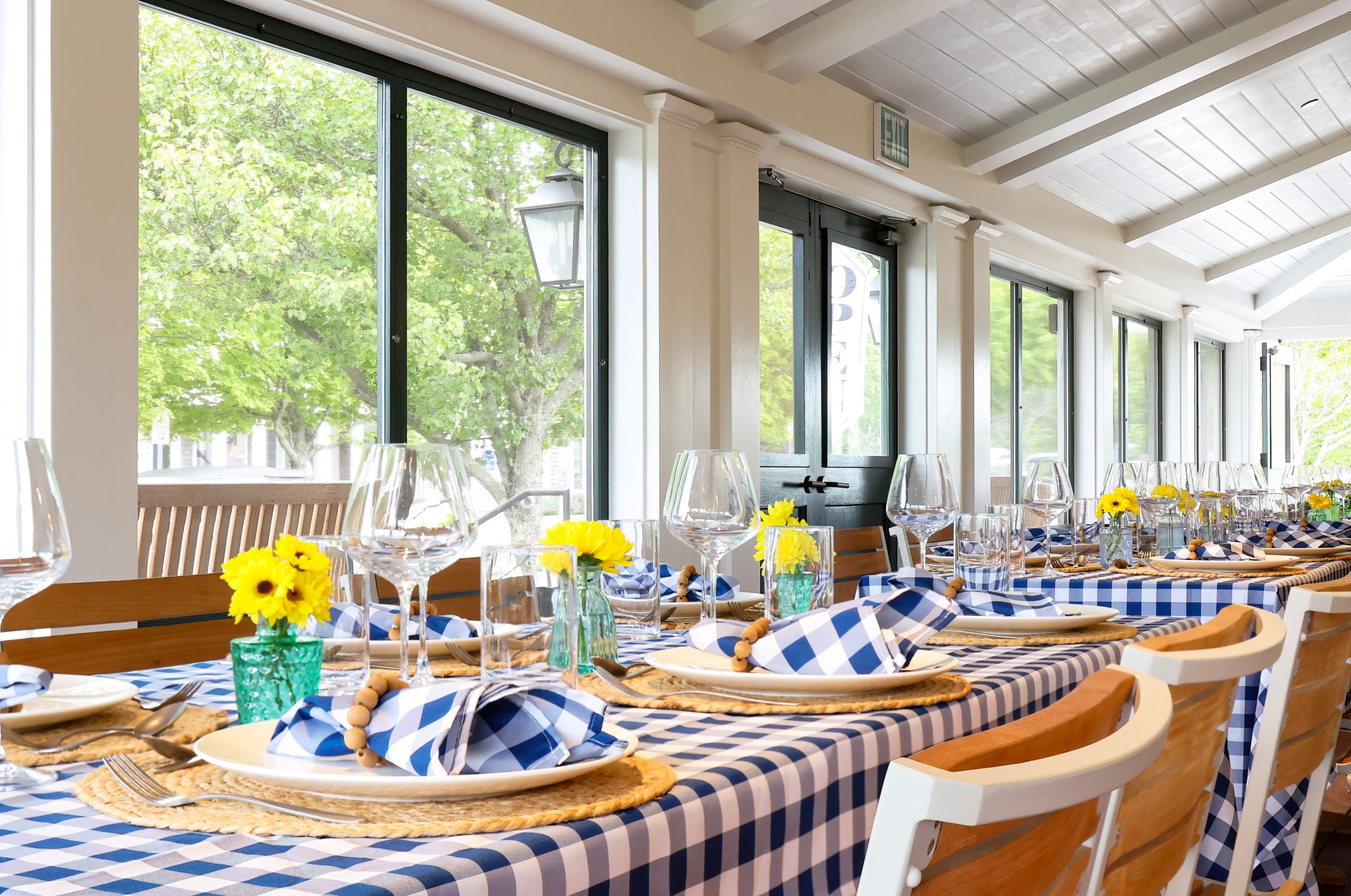 A table set with blue gingham linens and yellow flowers on The Hive porch
